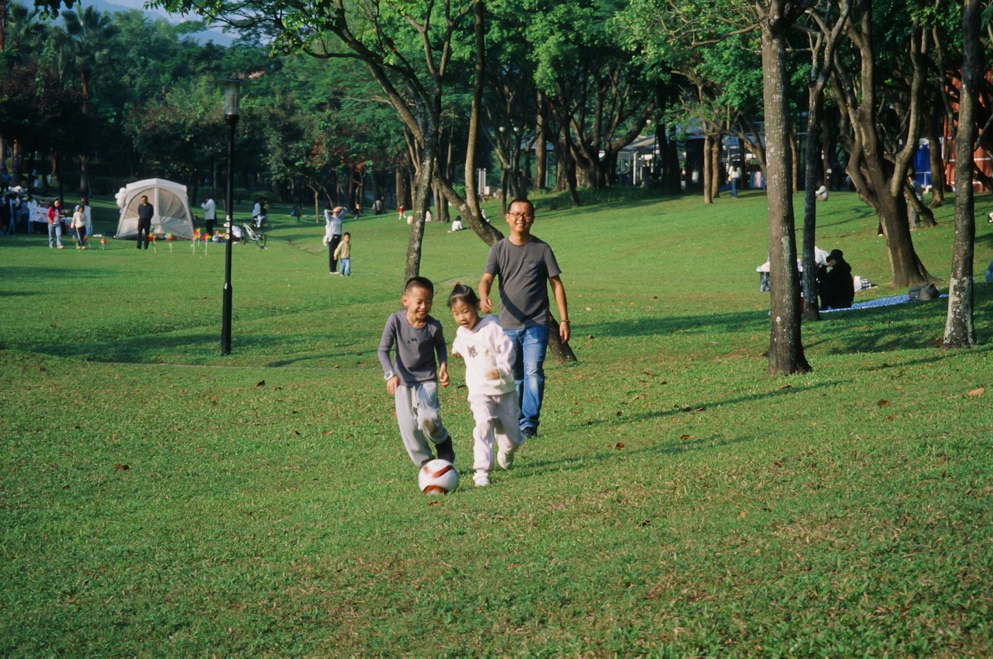 Een man en twee kinderen die op een grasveld in het park voetballen.